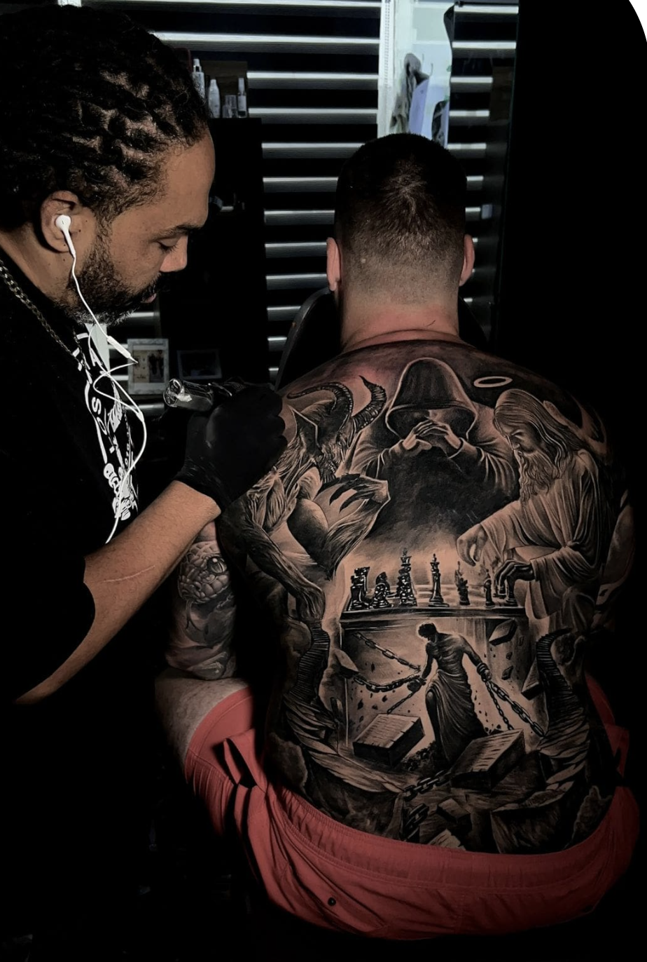 Tattoo artist working on a detailed full-back black and gray realism piece